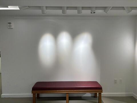 a blank wall with three lights and a bench