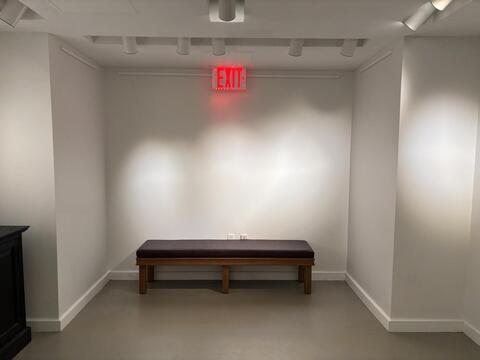 a white wall with three lights, bench, and exit sign